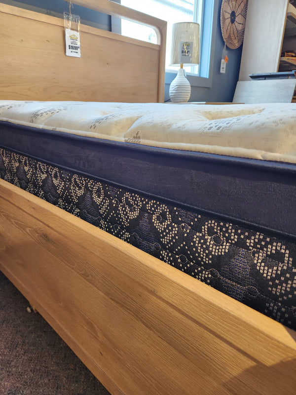 The KingsDown Ingleside ET Plush Mattress with a light wood frame is displayed in a stylish, well-lit showroom.