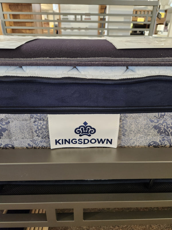 A KingsDown Mallory ET Firm Mattress with blue and white patterns sits on a metal frame, featuring tri-zone pocket coils.