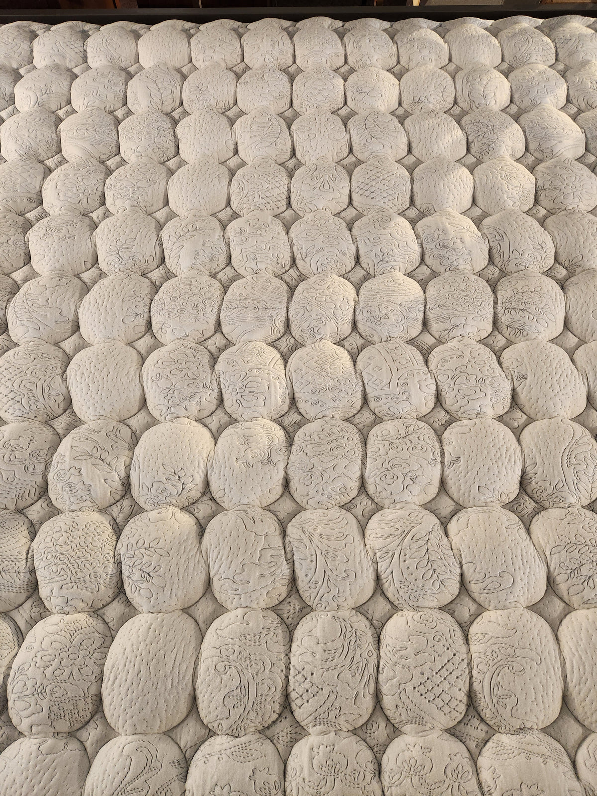 Close-up of KingsDown Mallory ET Firm Mattress surface with oval quilting, stitched detail, and cooling gel foam layers.