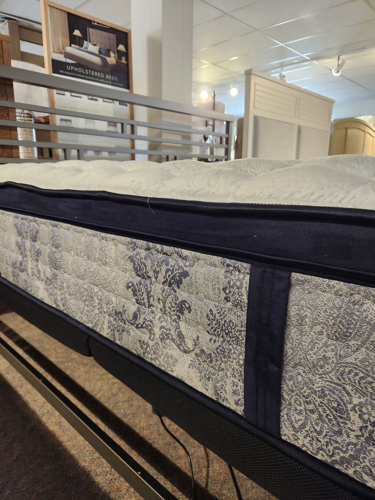 A close-up of the KingsDown Mallory ET Firm Mattress with patterned fabric and cooling gel foam on display in a showroom.