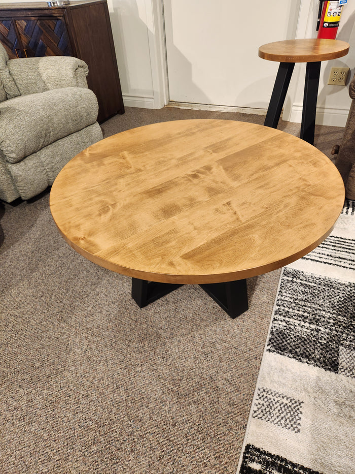 Handstone Belmont Round Coffee Table with light finish and black legs, shown on a carpeted floor.