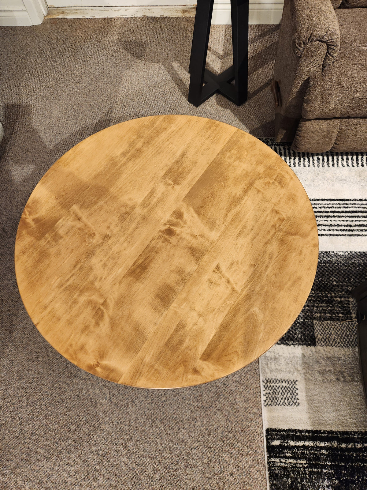 The Belmont Round Coffee Table by Handstone stands on a carpeted floor near a rug and upholstered furniture.