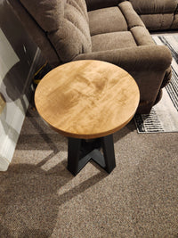 A Handstone Belmont Round Chairside Table with a black base is beside a brown recliner on a carpeted floor.