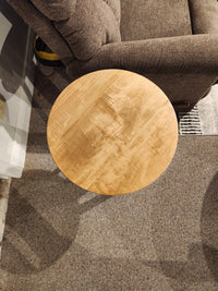 A Handstone Belmont Round Chairside Table sits next to a brown upholstered chair on a carpeted floor.