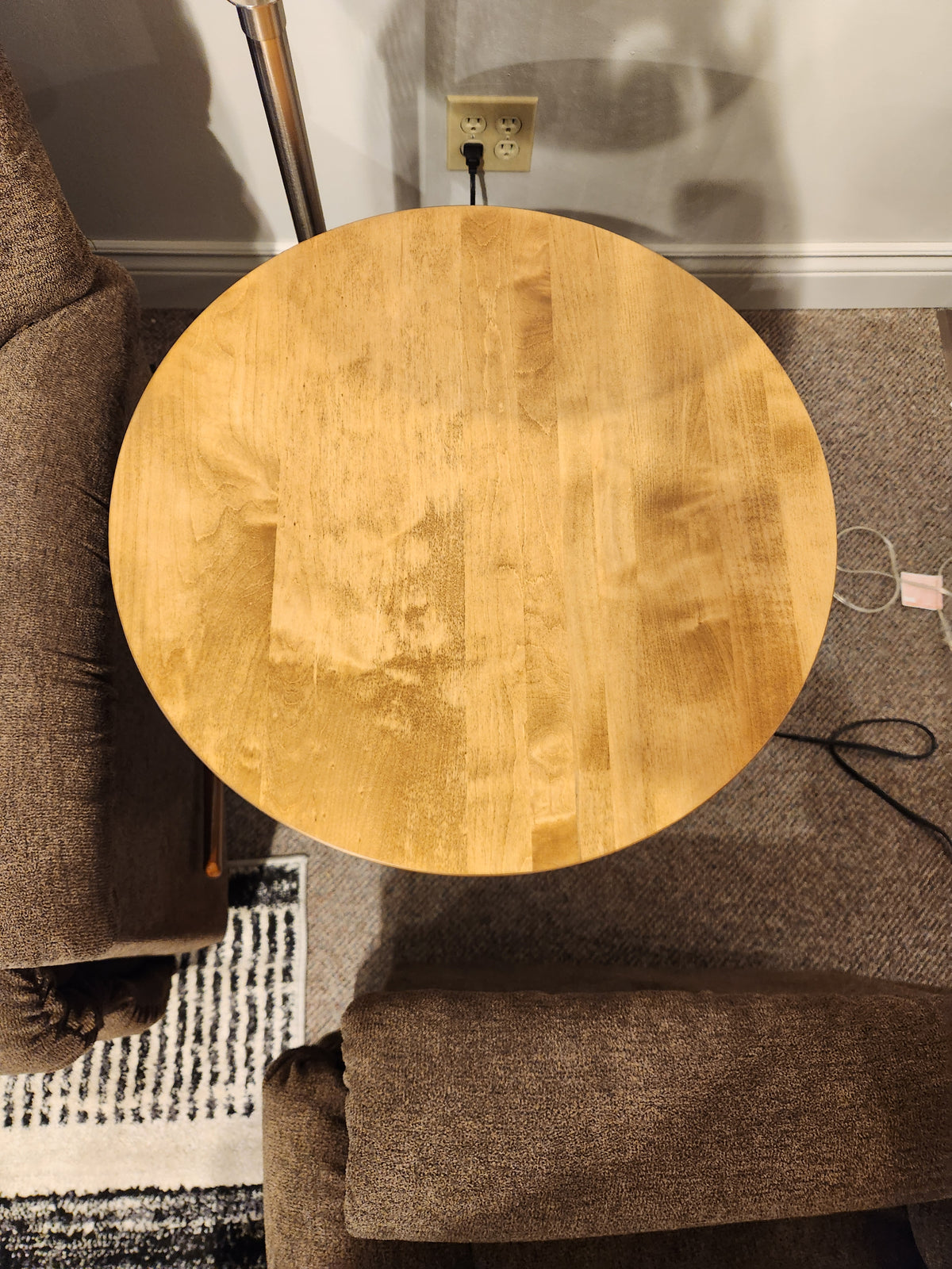 Belmont Round End Table by Handstone between two brown chairs, viewed from above with nearby cords and outlet.