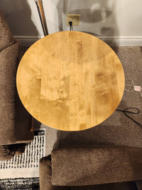 Belmont Round End Table by Handstone between two brown chairs, viewed from above with nearby cords and outlet.