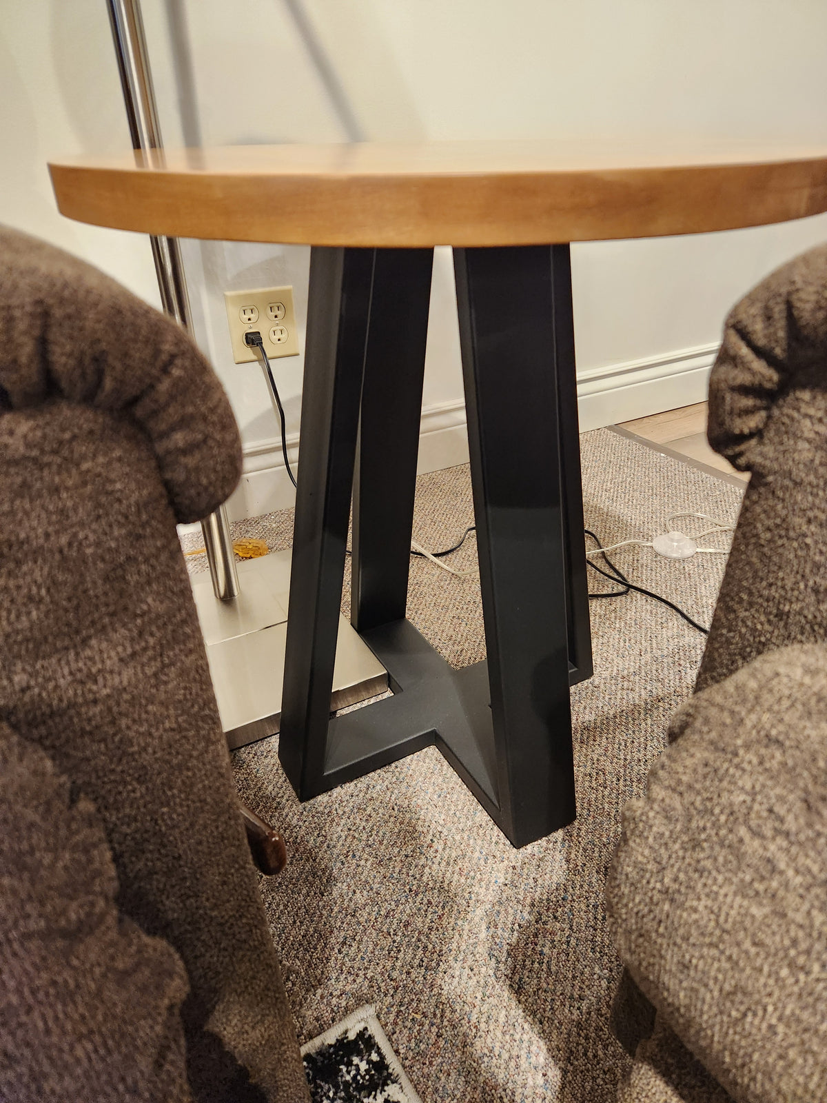 A Handstone Belmont Round End Table with a black metal base sits between two brown upholstered chairs.
