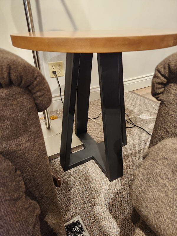 A Handstone Belmont Round End Table with a black metal base sits between two brown upholstered chairs.