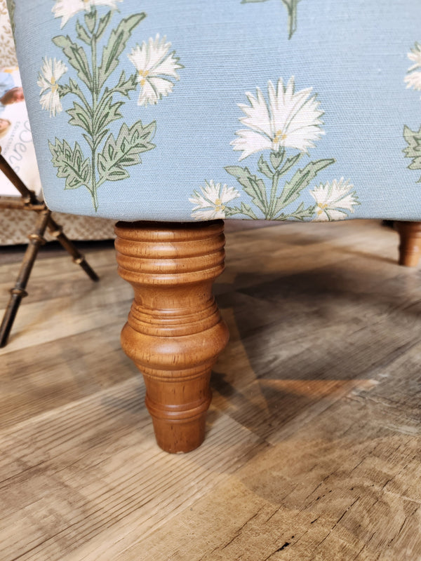 Close-up of Arden Club Chair leg by Best, attached to blue, button-tufted floral fabric on a wooden floor.