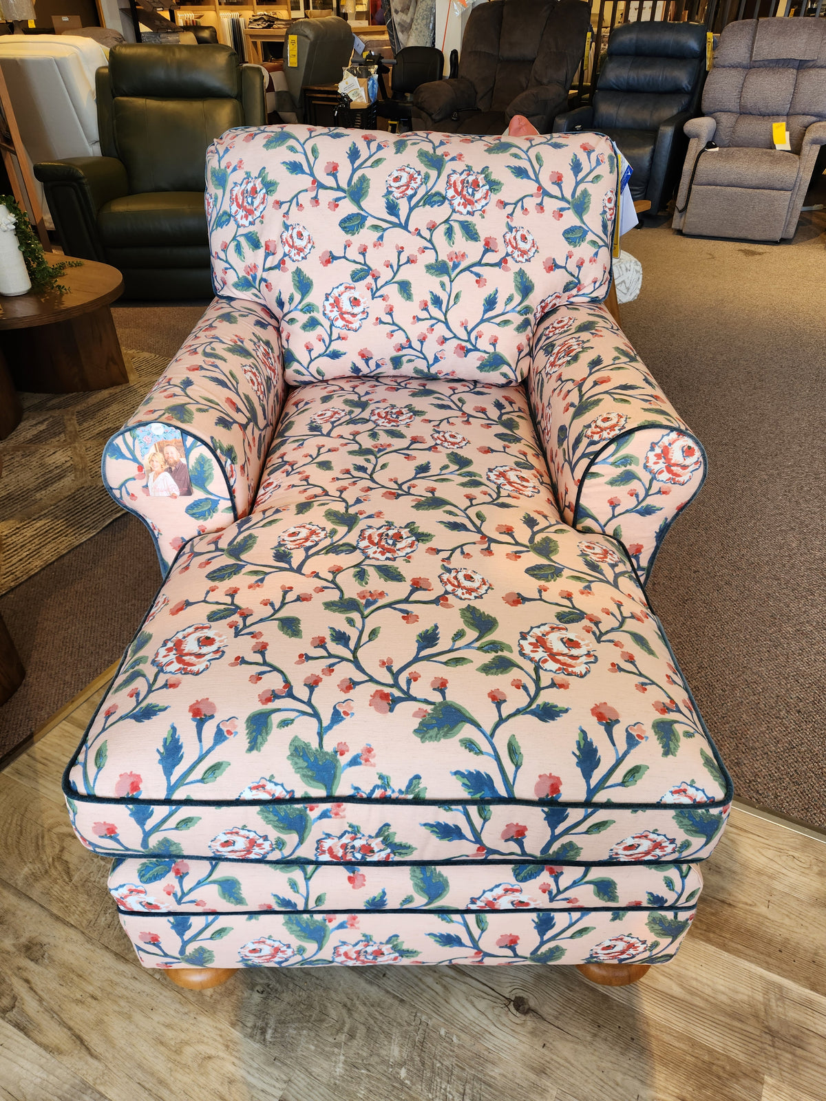 The Kress Chaise Lounge by Best features pink floral fabric, blue trim, and wooden legs for an heirloom-inspired charm.