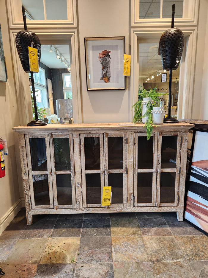 The Jofran 2125 Rustic Shores 6 Door Accent Cabinet with glass doors sits between black lamps in a rustic showroom.