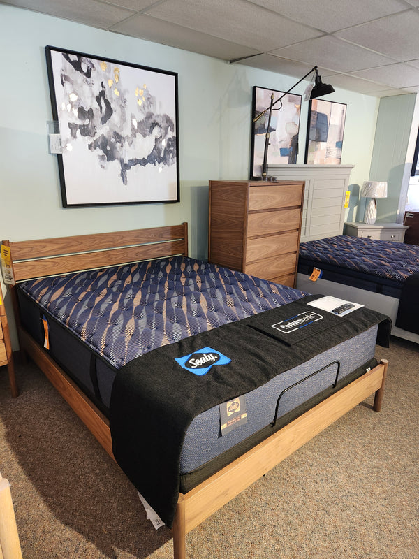 A Sealy Riva TT Firm Hybrid 1300 Coil Copper Series mattress on a wooden frame, beside a dresser and wall art.