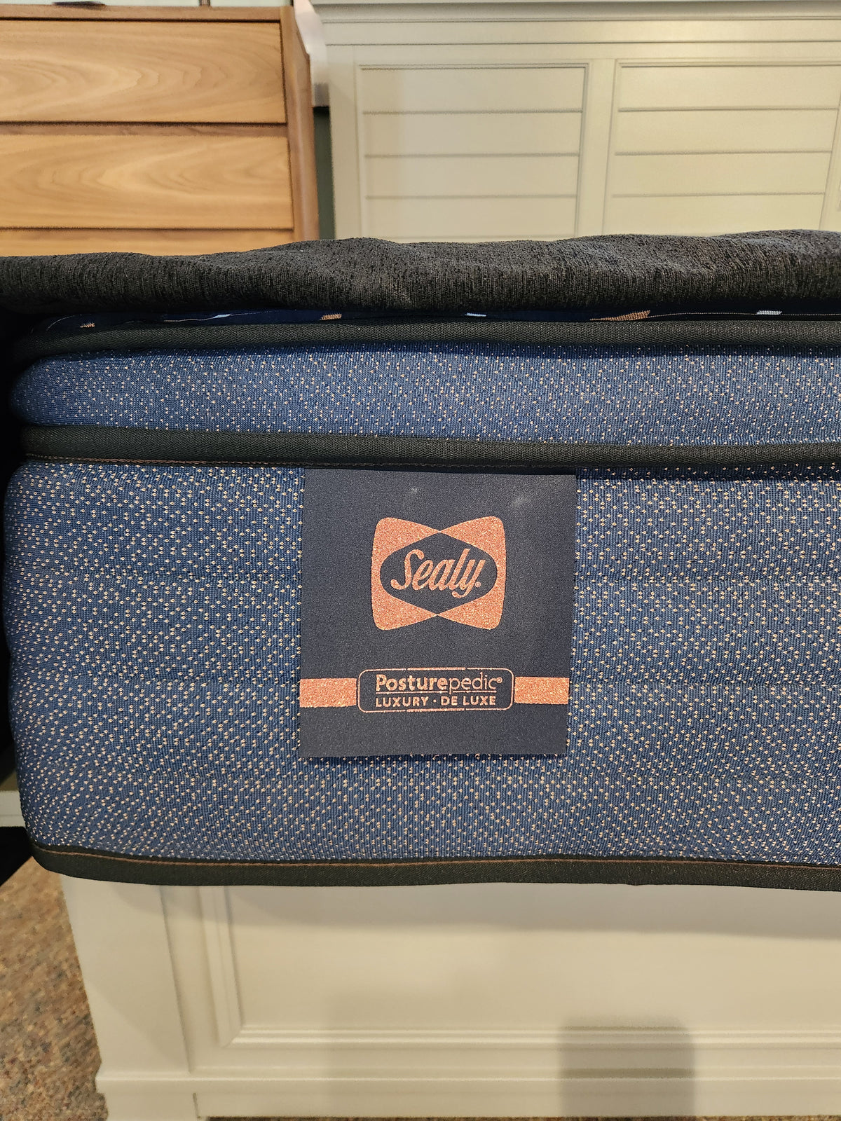 Close-up of a Sealy Rowan ET Medium 1300 Coil Copper Series mattress corner with logo tag on a blue, cooling surface.