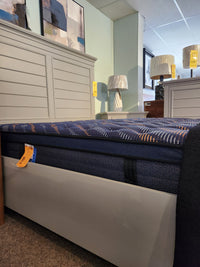 The Sealy Rowan ET Medium 1300 Coil Copper Series mattress on a light gray bed frame, with lamps and paintings nearby.