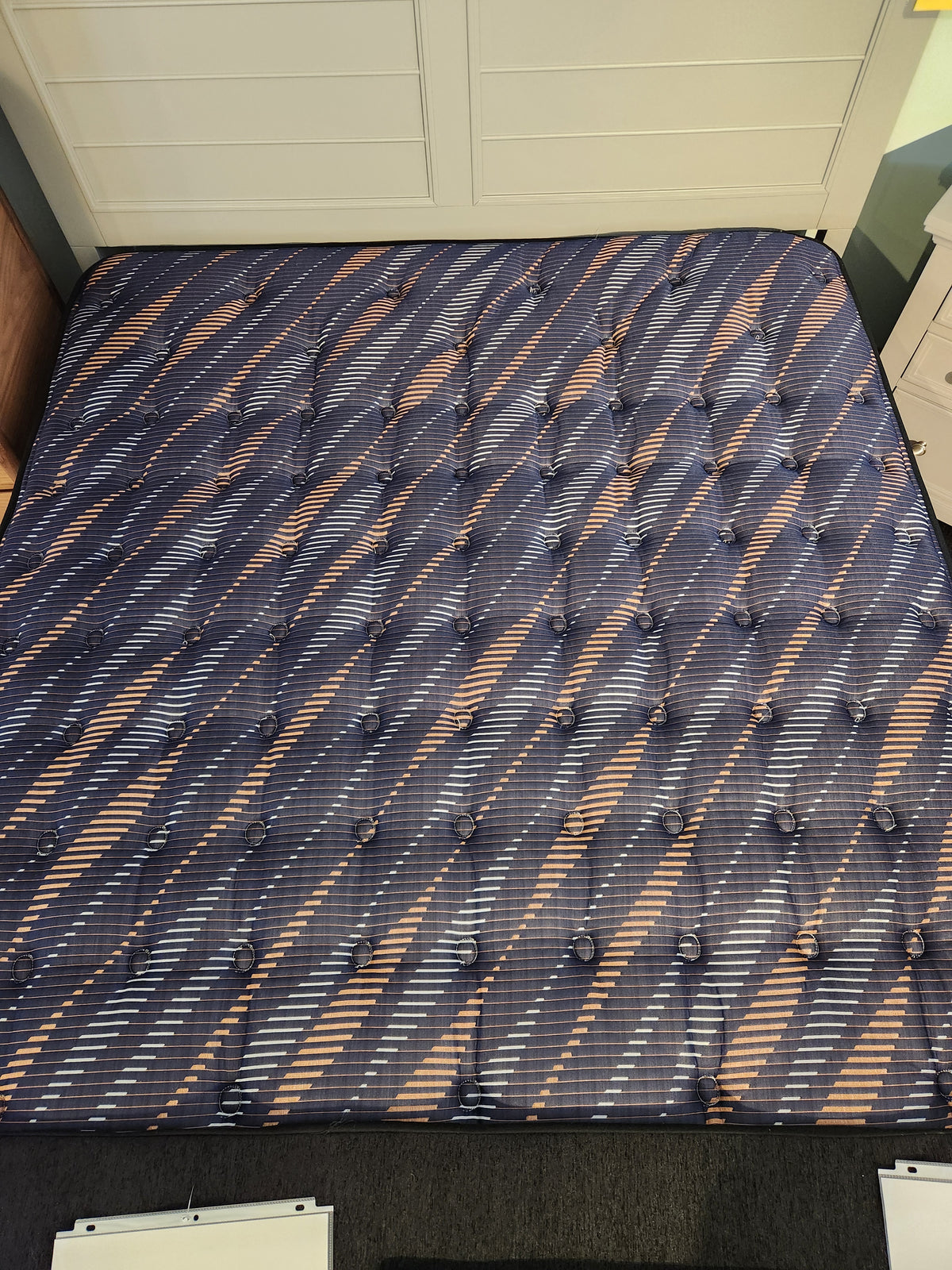 The Sealy Rowan ET Medium 1300 Coil Copper Series mattress sits on a black carpet near white drawers and cabinets.