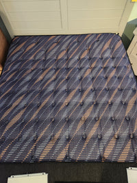 The Sealy Rowan ET Medium 1300 Coil Copper Series mattress sits on a black carpet near white drawers and cabinets.