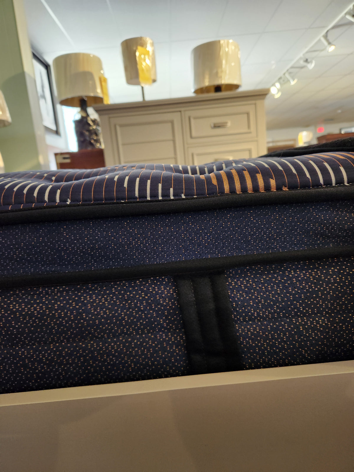 A close-up of the Sealy Rowan ET Medium 1300 Coil Copper Series mattress with patterned cover in a furniture store.
