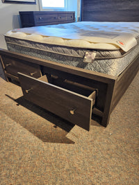 The Magnussen B6308 Merrifield Queen Storage Bed with oak veneer and drawers is set on a carpeted floor.