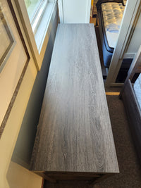 A Magnussen B6308 - Merrifield dresser in gray oak stands between the window and bed in this modern bedroom display.