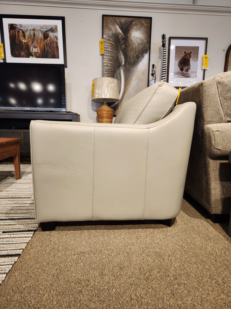 Side view of a Leather Craft Sophia Loveseat in light gray Canadian leather, with animal art and a lamp in the background.