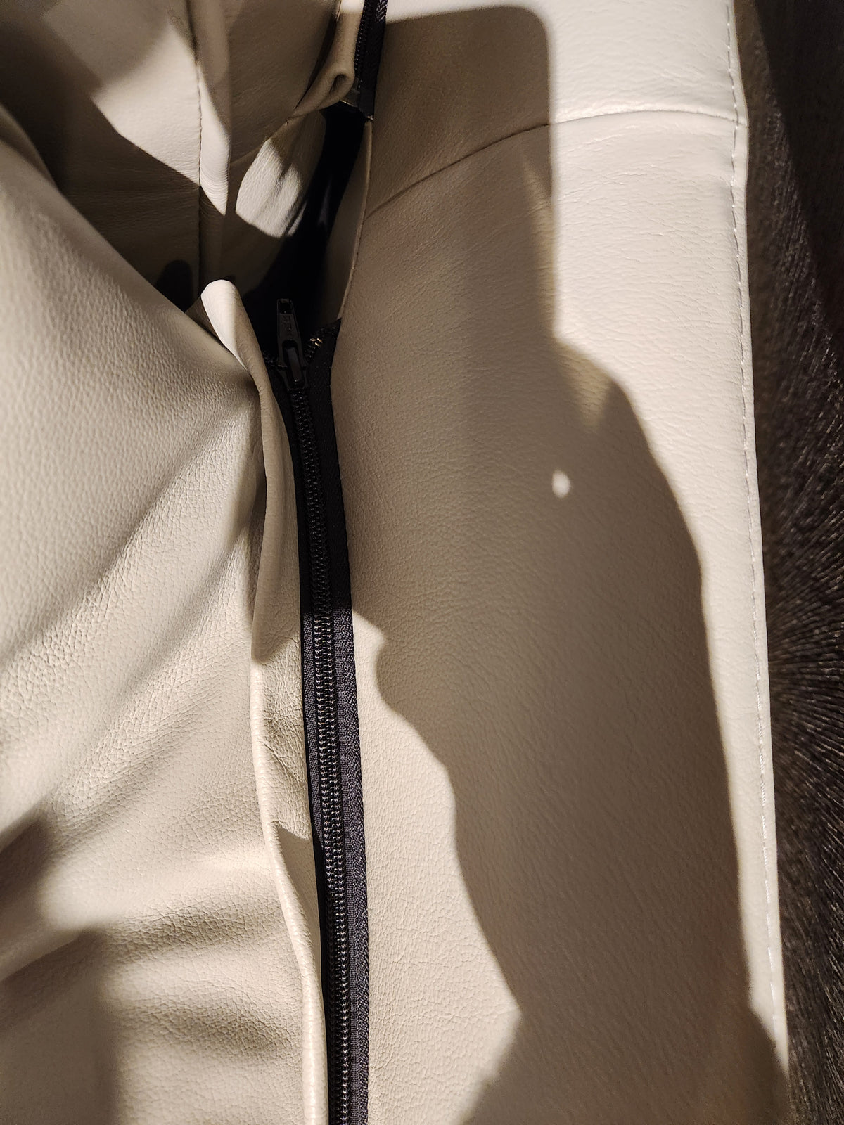 A close-up of Canadian leather on the Leather Craft Sophia Sofa features a black zipper and shadow on the material.