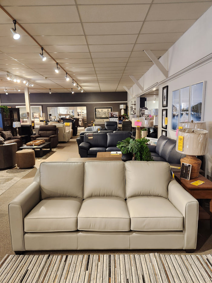 The Leather Craft Sophia Sofa in beige is displayed in a showroom with other sofas and Canadian leather decor.