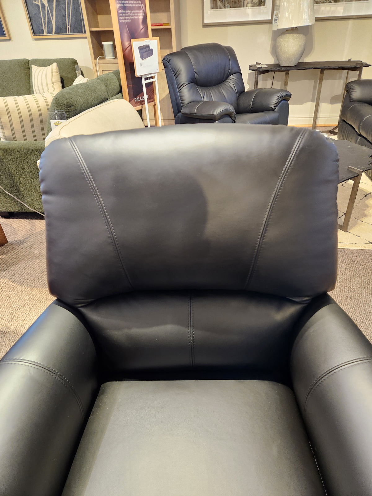 Close-up of a black Leather Craft 698 Reclining Chair in a showroom, with other Canadian leather pieces in the background.