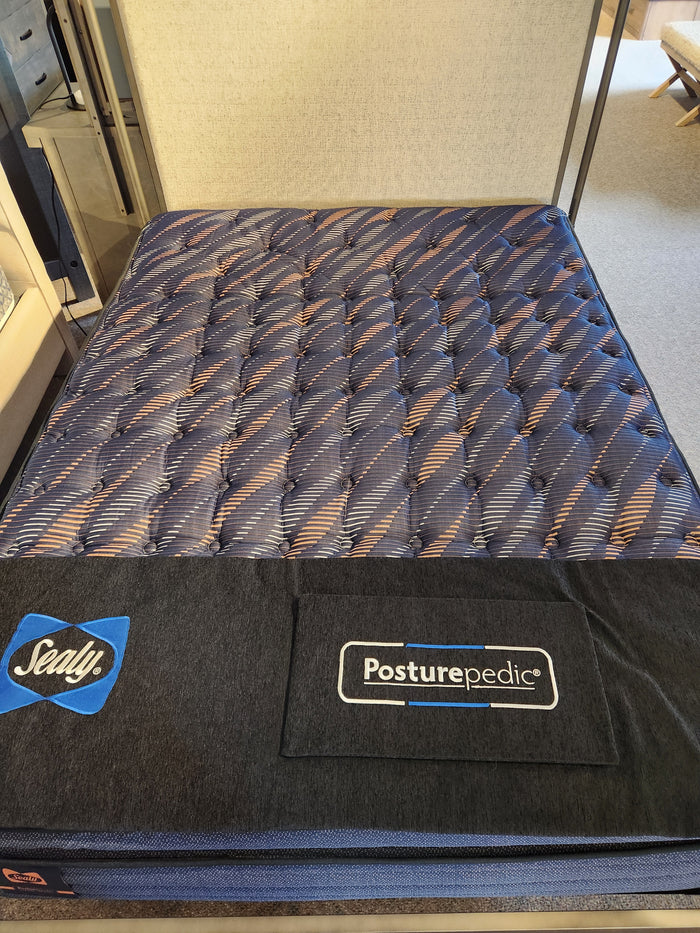 A Sealy Roux ET Soft 1300 Coil Copper Series mattress with a blue and black top displayed in a showroom.
