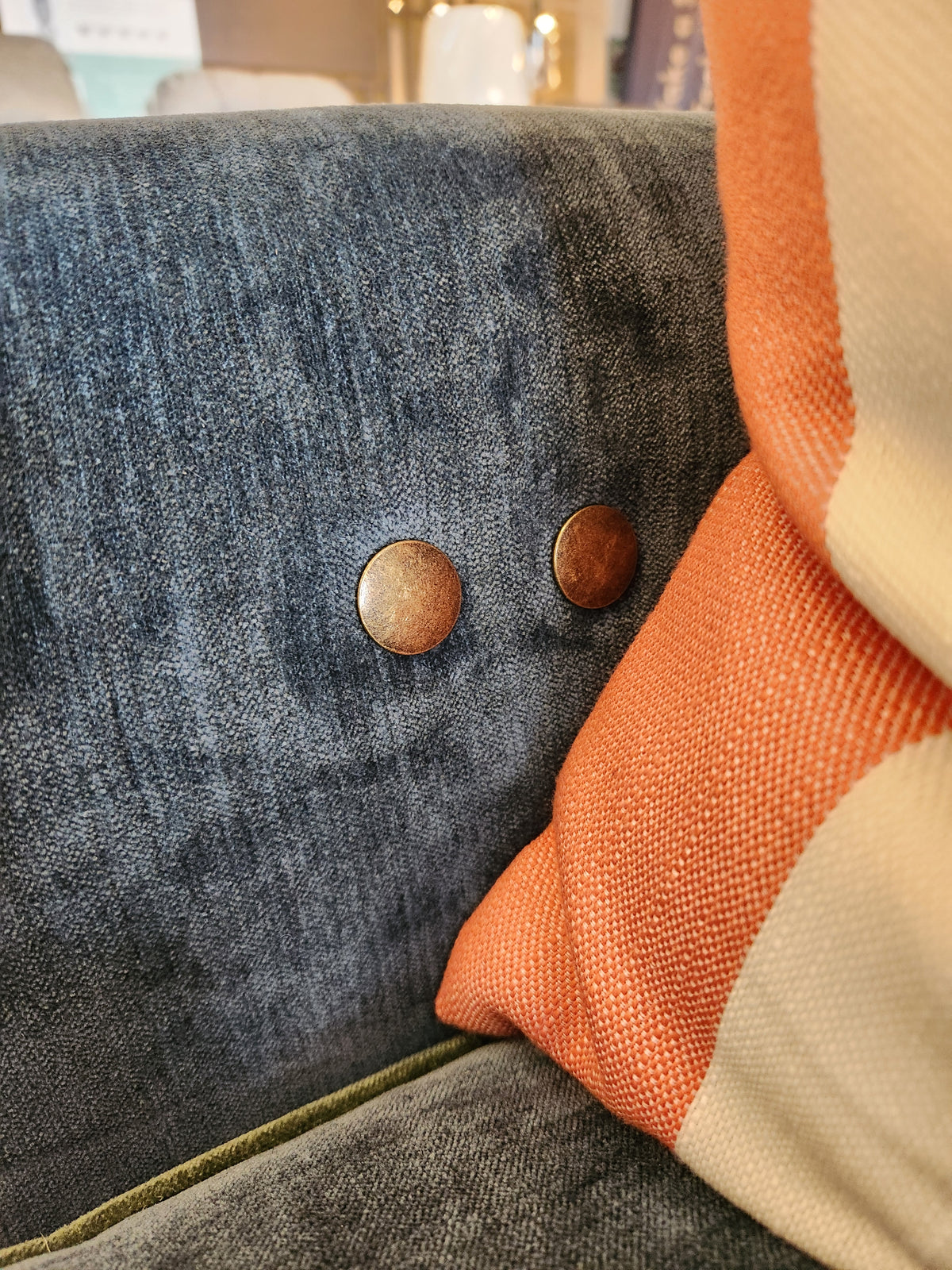 Close-up of the Adeline Sofa by Best, featuring blue upholstery, metal buttons, and an orange-white striped cushion.