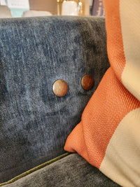 Close-up of the Adeline Sofa by Best, featuring blue upholstery, metal buttons, and an orange-white striped cushion.