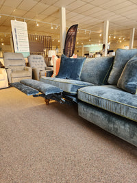 The Adeline Sofa by Best, a blue sectional with reclined footrest and reversible cushions, is shown in the showroom.