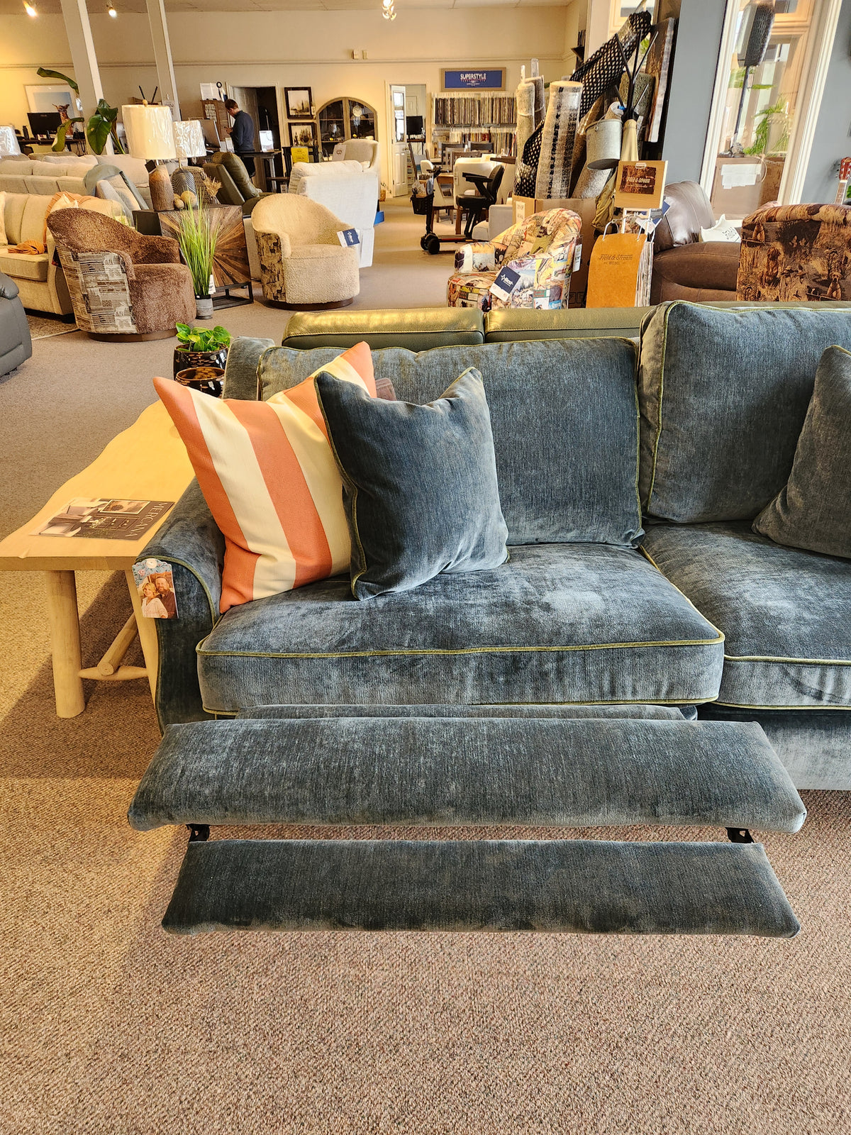 The Adeline Sofa by Best is a blue velvet incliner with striped pillows and pull-out footrests in the showroom.