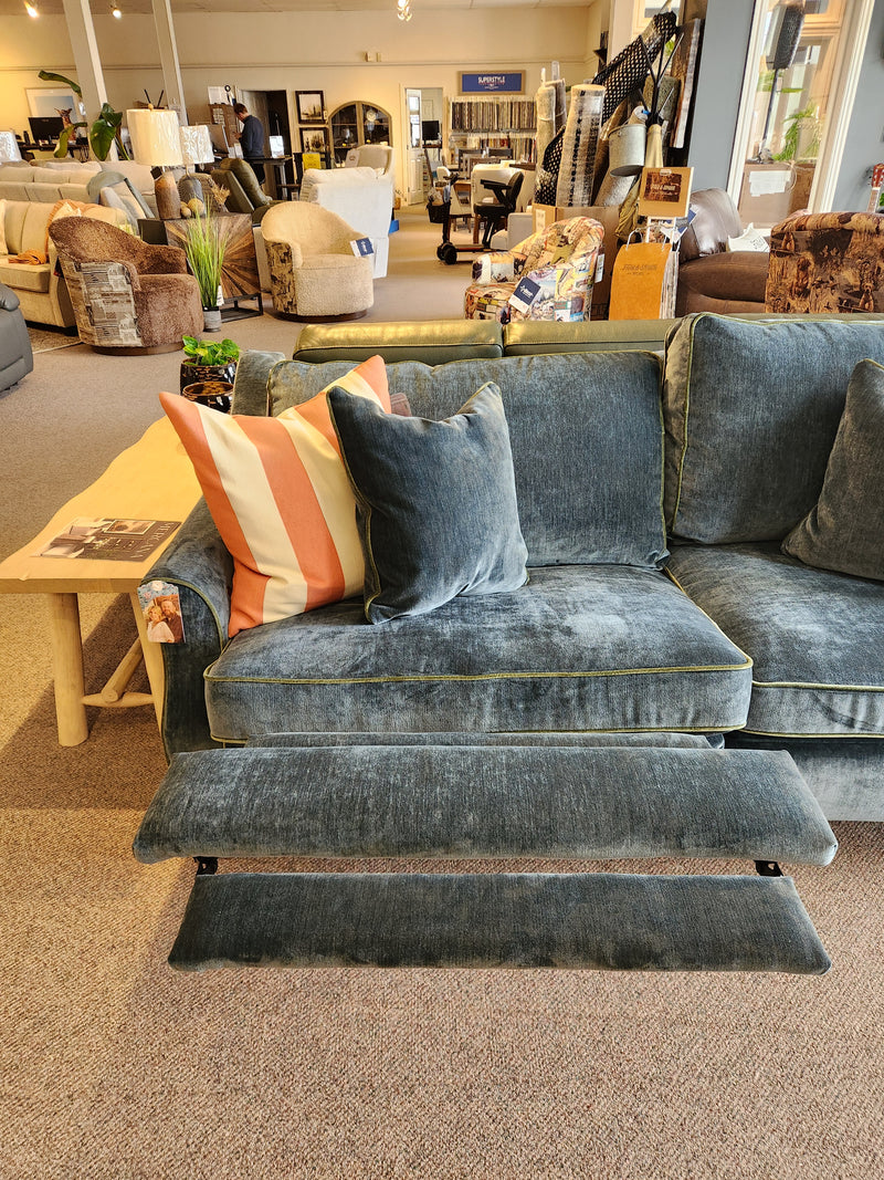 The Adeline Sofa by Best is a blue velvet incliner with striped pillows and pull-out footrests in the showroom.