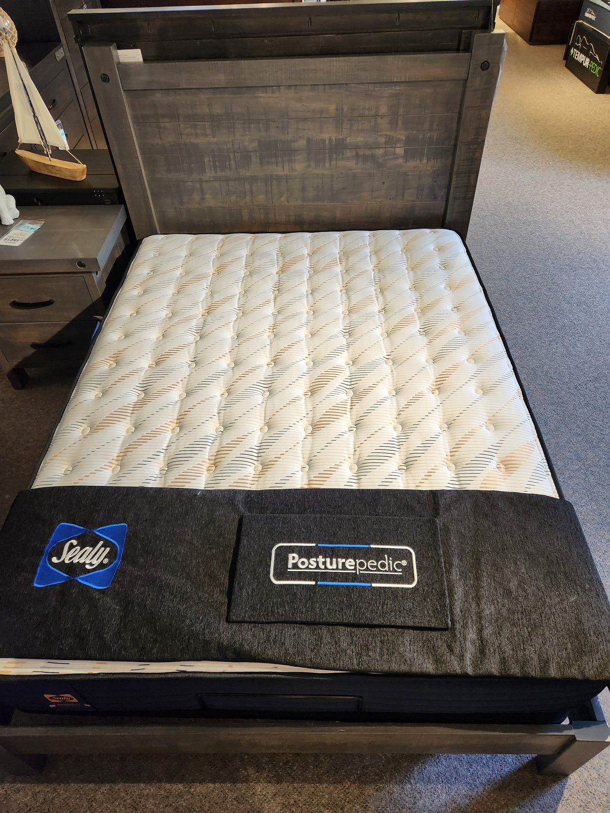 A Sealy Cyra TT Firm 1000 Coil Copper Series mattress on a wooden bed frame by a nightstand in a showroom.