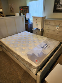 A showroom display features a queen Springwall Michelle ET Medium Mattress on a light bed frame with dressers and a lamp.