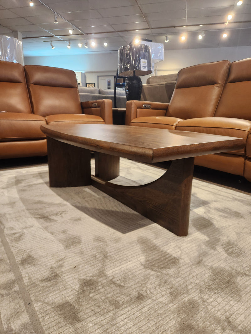 The Magnussen T6385 Phoebe Rectangular Cocktail Table in Sienna Brown sits on a carpet between tan leather sofas.