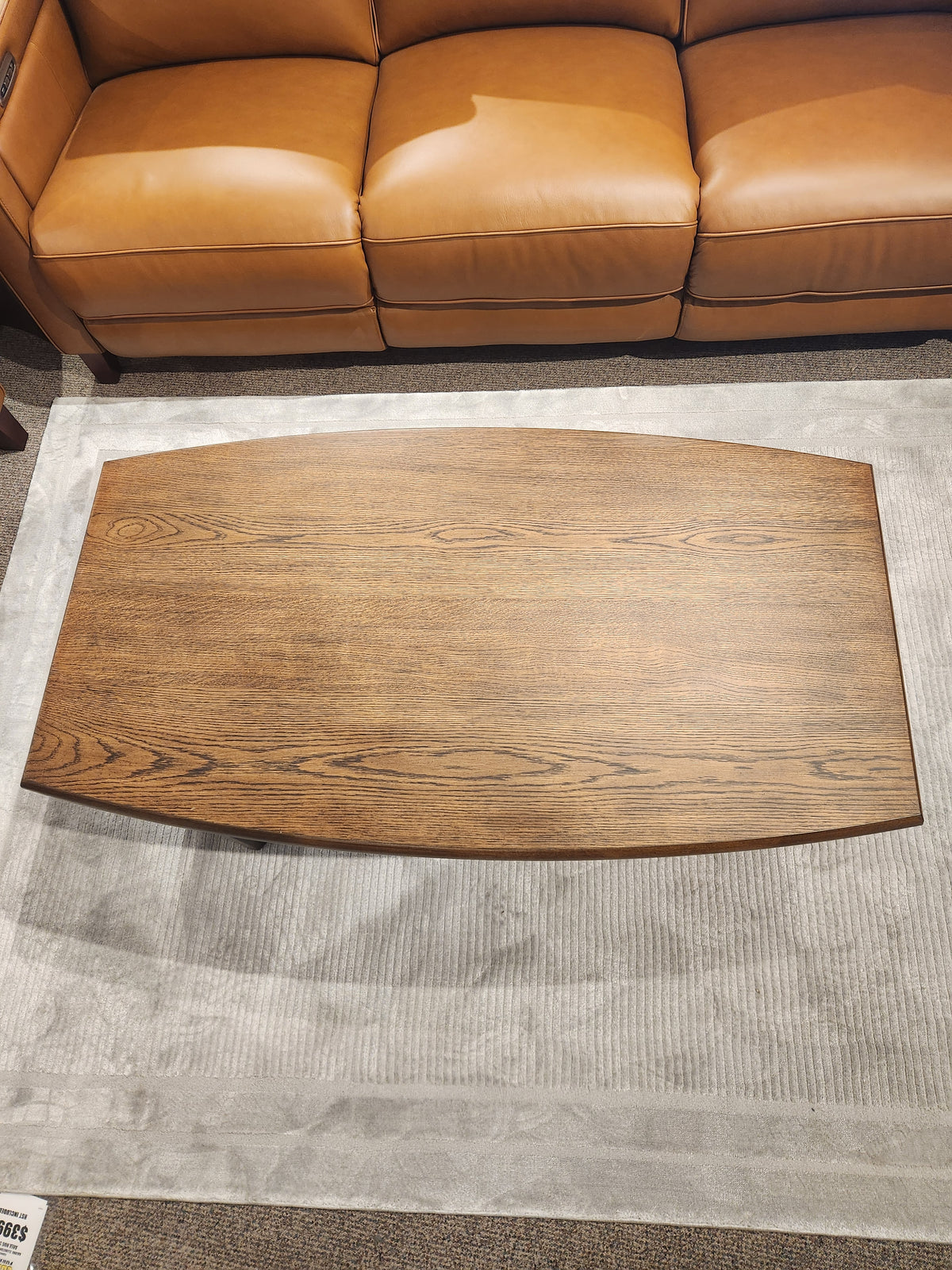 The Magnussen T6385 - Phoebe Rectangular Cocktail Table sits on a gray rug before a sienna brown leather sofa.