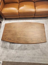 The Magnussen T6385 - Phoebe Rectangular Cocktail Table sits on a gray rug before a sienna brown leather sofa.