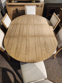 The Magnussen D6480-Coventry 7pc Dining Set features an oval wooden table and six beige upholstered chairs.
