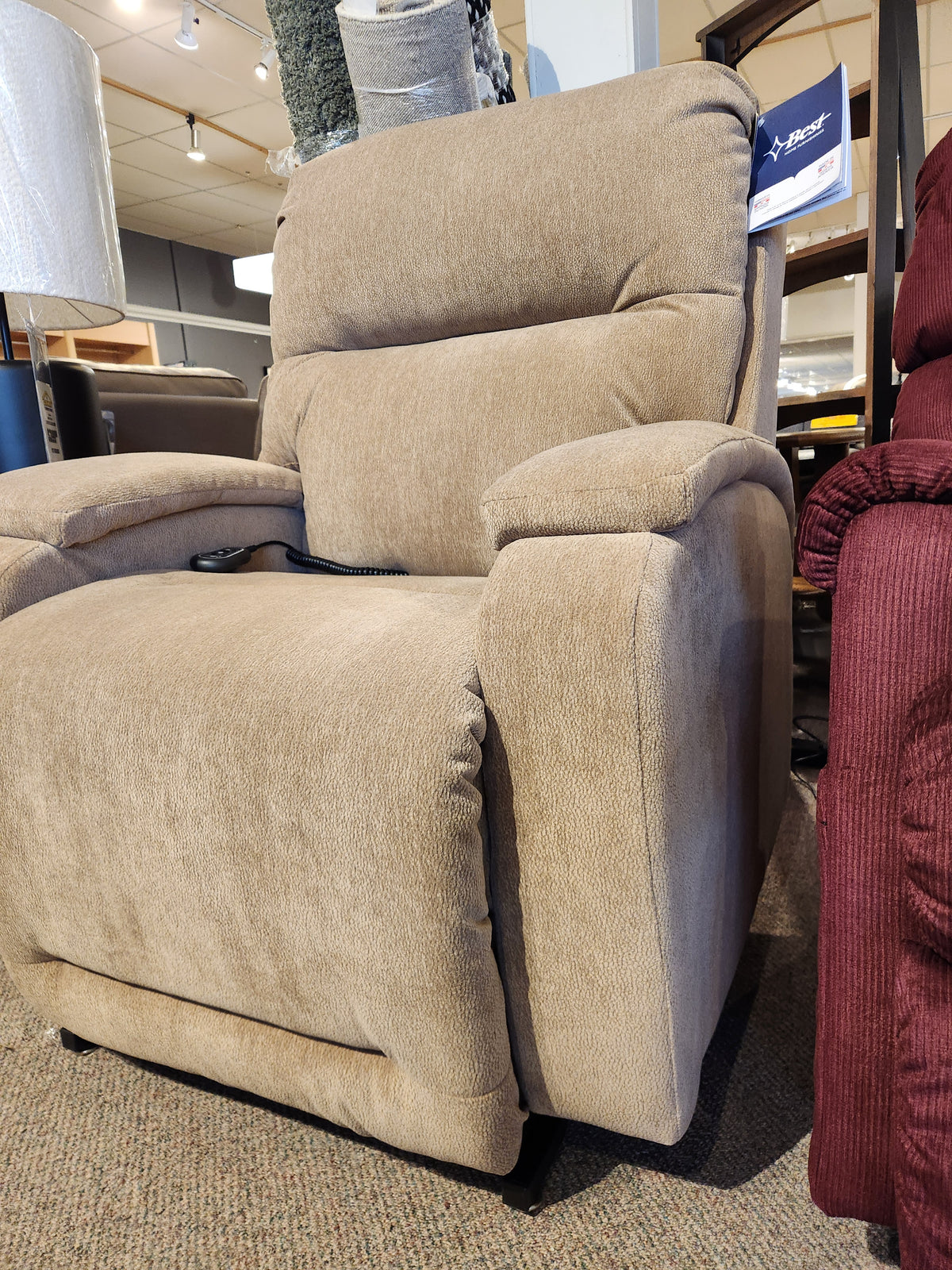 A beige Best Maverly 9N11 Lift Chair with padded arms and wired remote is on display in the furniture store showroom.