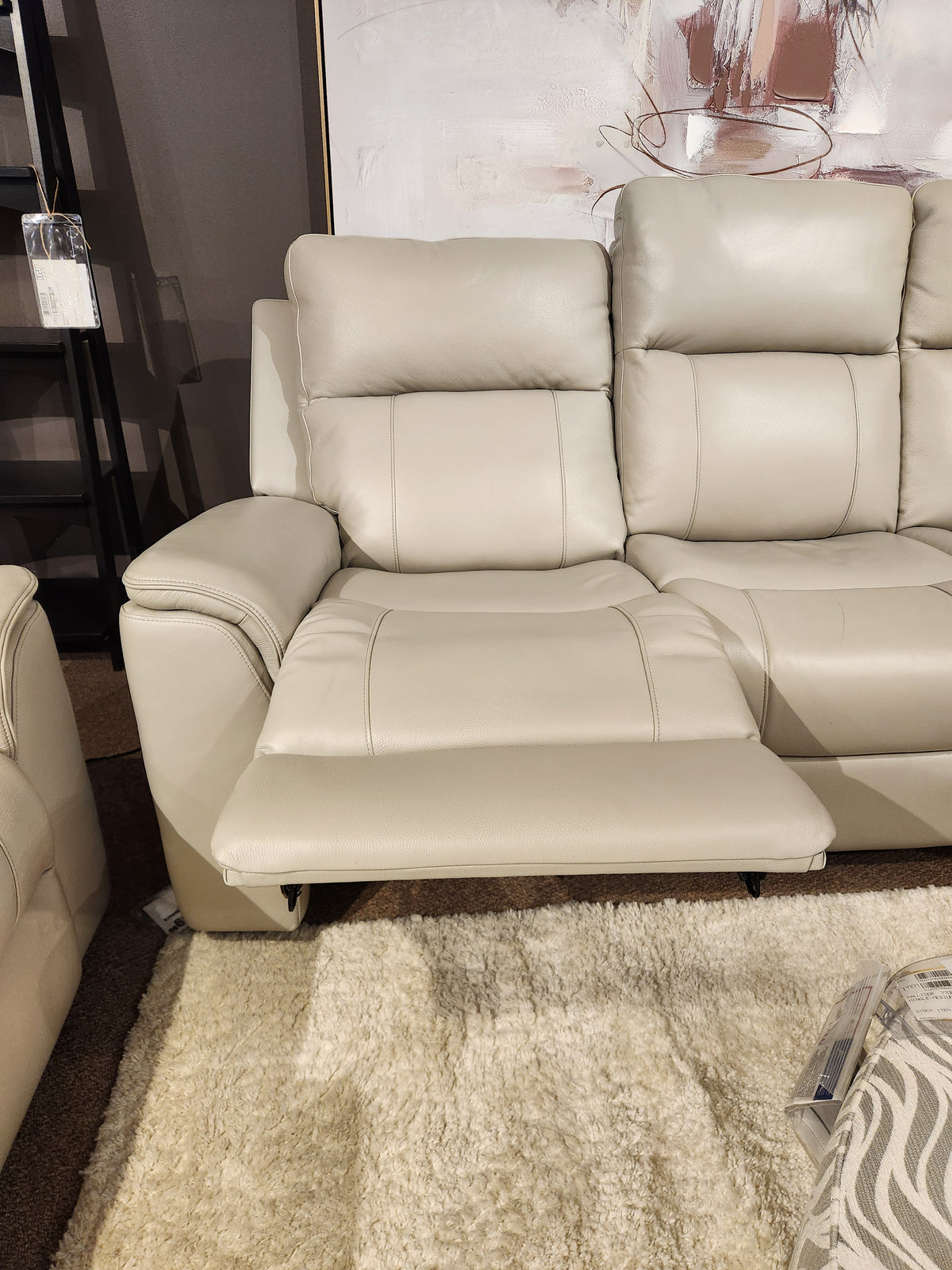 The 16 WEST Austin Power Recliner Sofa-520157 with extended footrest is on a cream shag rug near modern art.