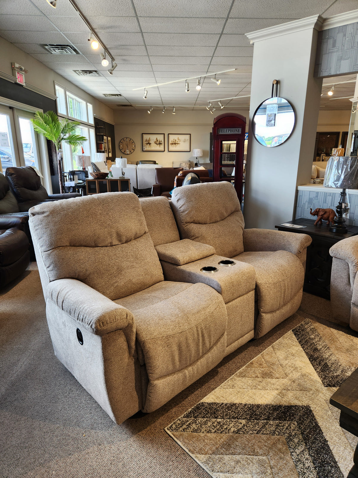 The 521 James Loveseat with console by La-z-boy, in beige, is showcased in a modern showroom setting.