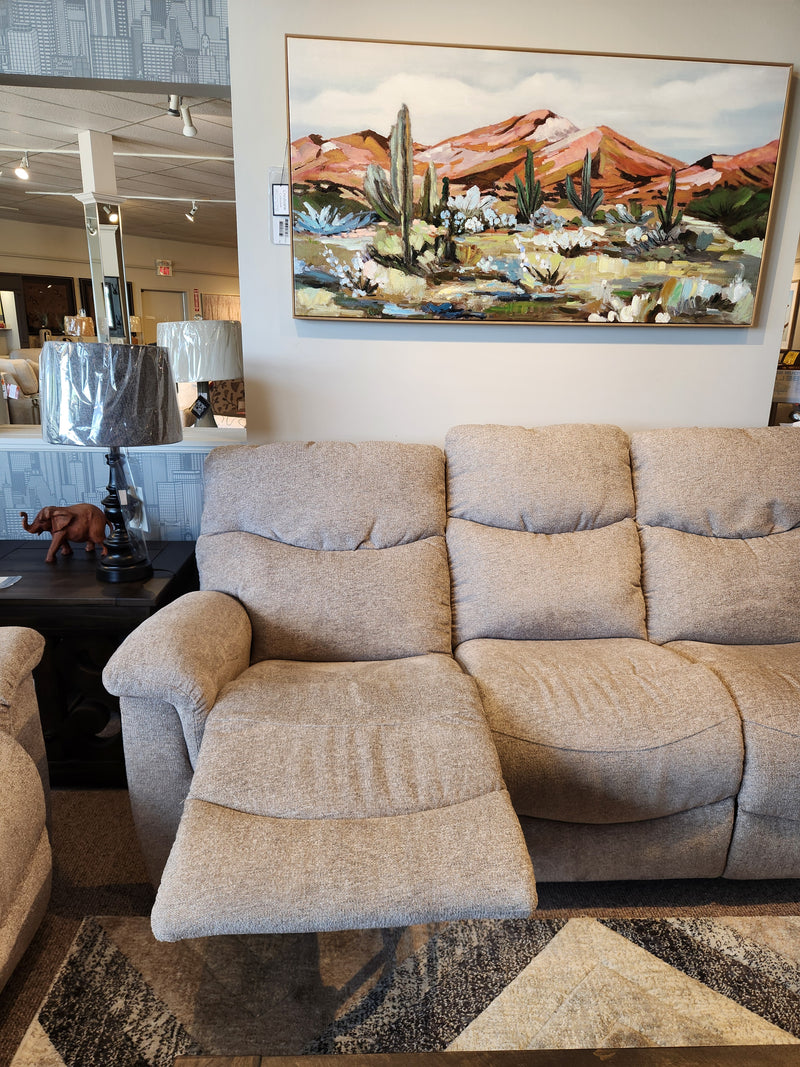 The La-z-boy 521 James Sofa, beige with footrest extended, paired with a lamp and landscape painting in a showroom.