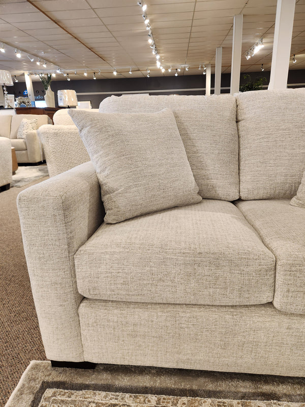 The Superstyle 9540 Stationary Loveseat with beige cushions is showcased in a modern, well-lit showroom.