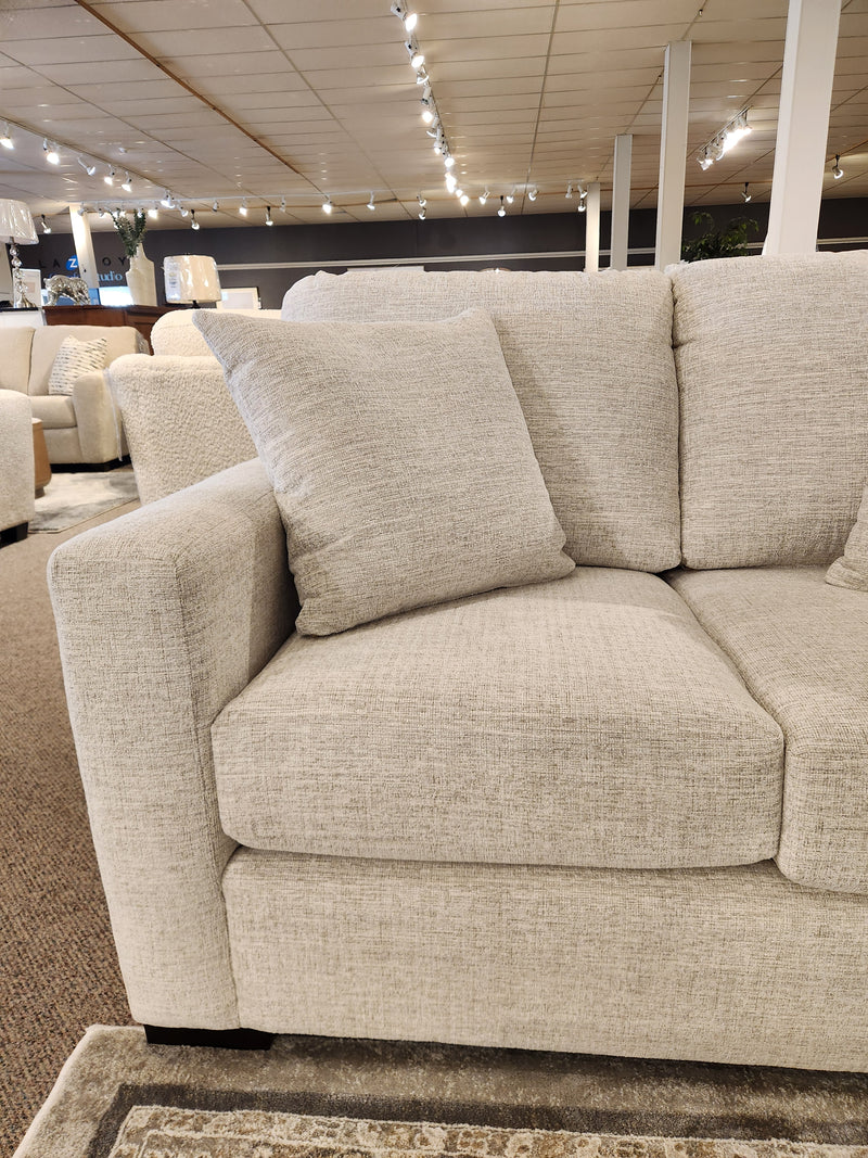 The Superstyle 9540 Stationary Loveseat with beige cushions is showcased in a modern, well-lit showroom.