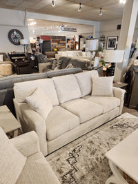 The Superstyle 9540 Stationary Sofa, beige with cushions, is shown in a store among other sofas and decor.