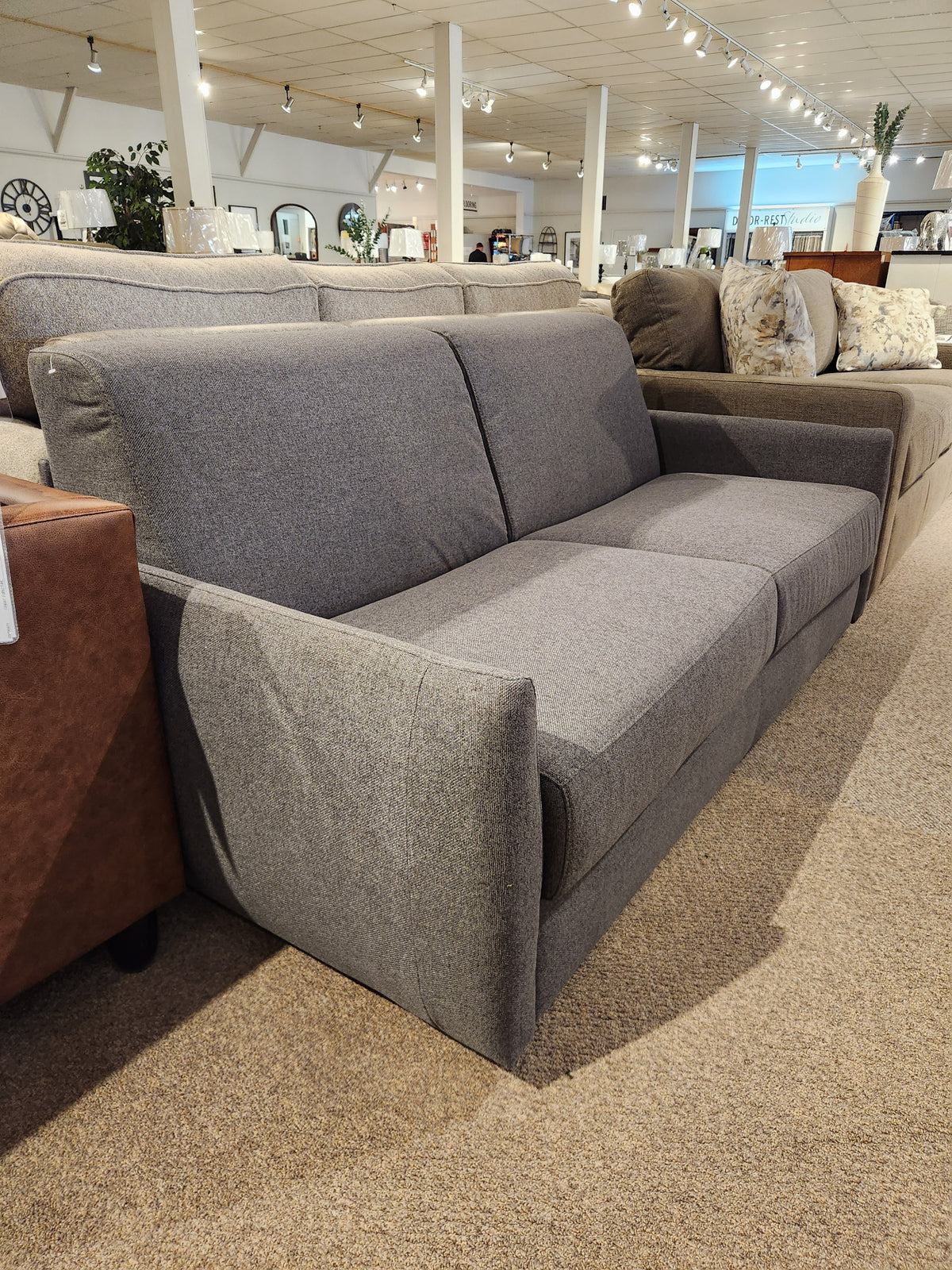 The Primo Vitale Sofa Bed in gray upholstery with Italian mechanism is displayed among other couches in the showroom.