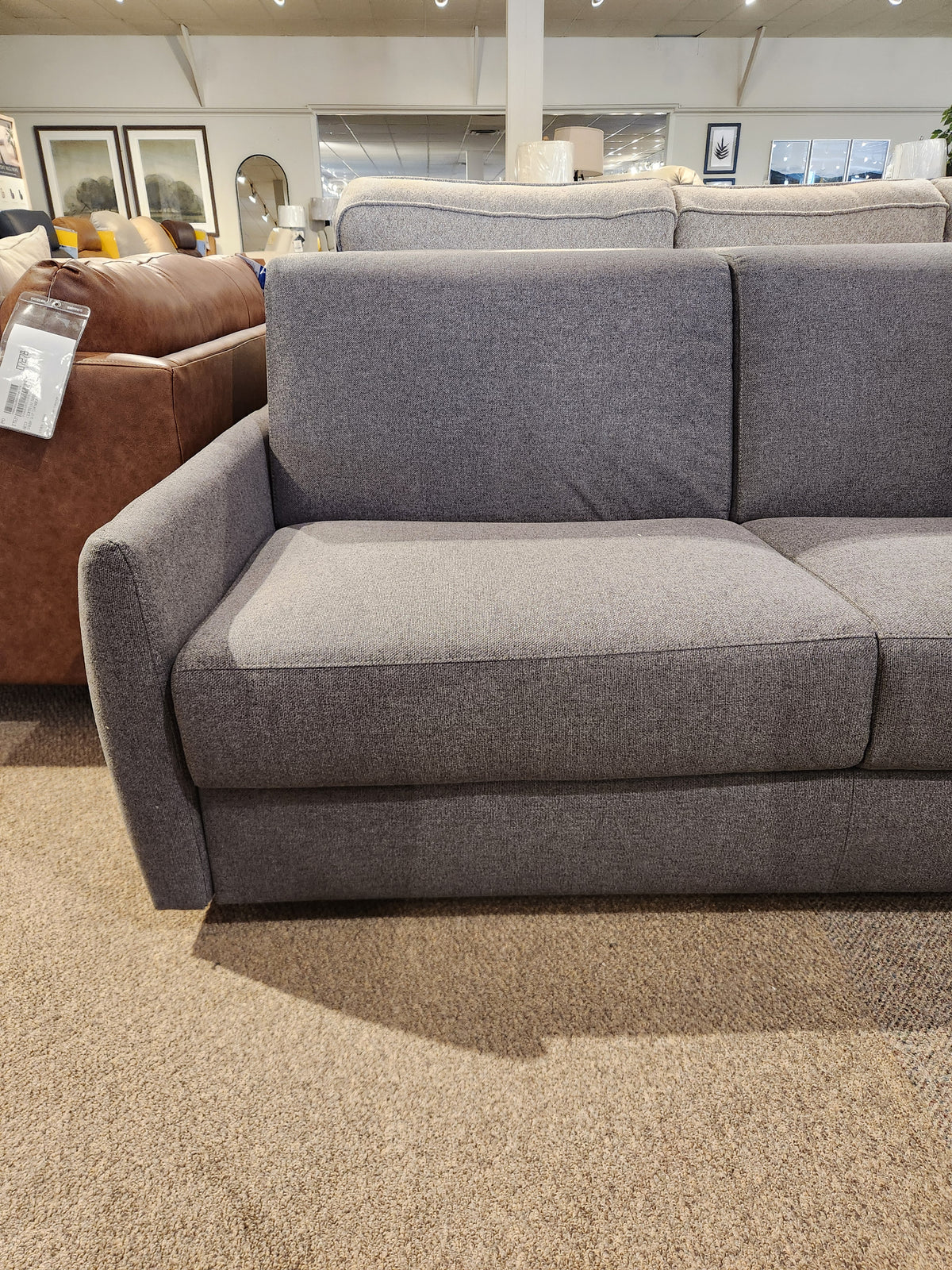 The Primo Vitale Sofa Bed in gray upholstery with memory foam is showcased on a beige carpet in the showroom.