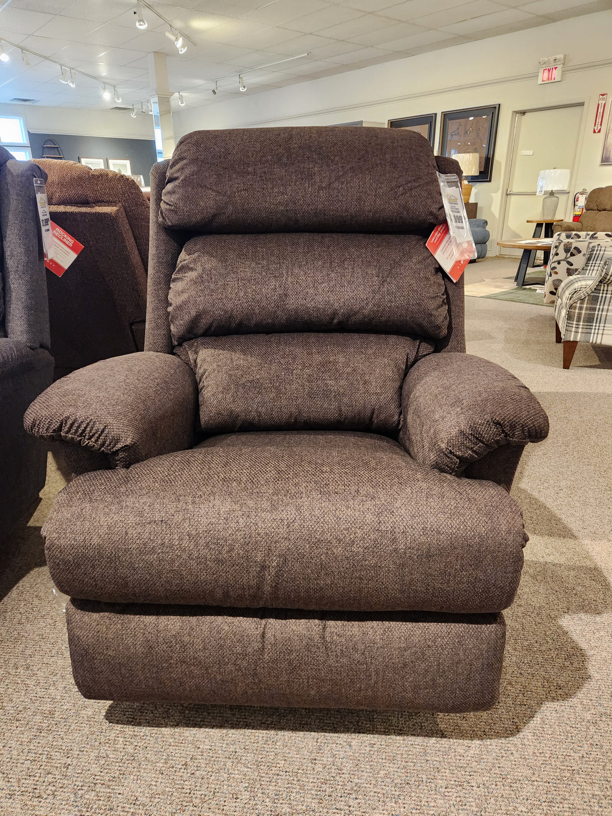 A tall La-z-boy 519 Astor Rocker Recliner with price tags on each arm is shown in a carpeted furniture showroom.