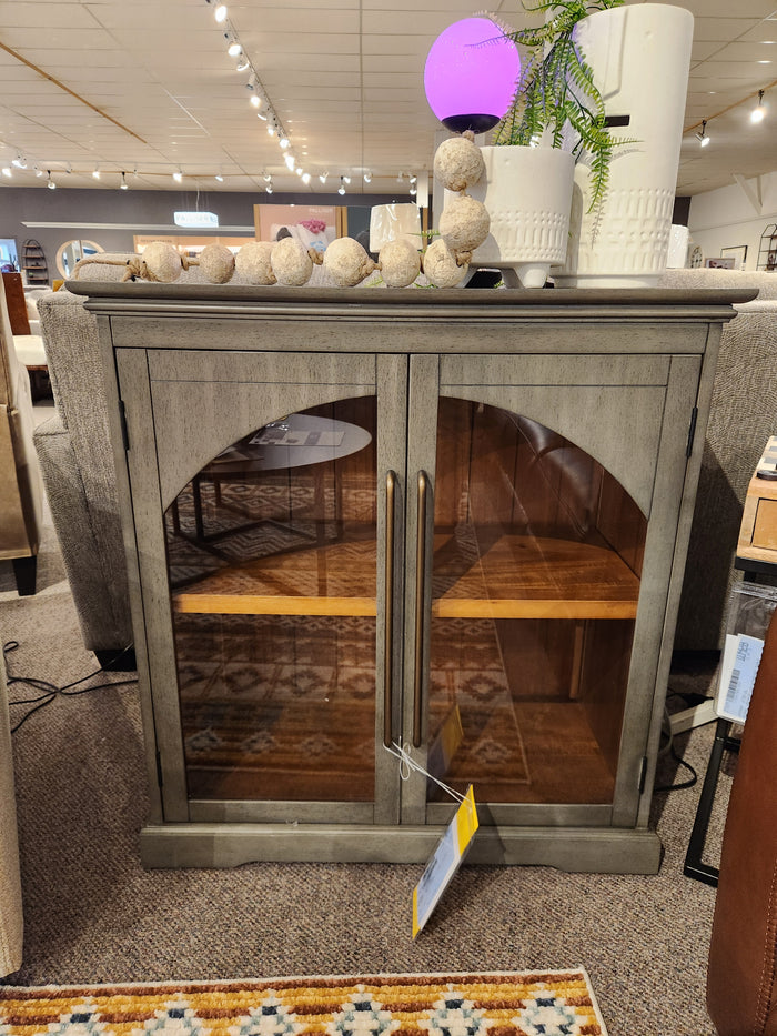 The Jofran 2294 Archdale Gothic Arch 2 Door Accent Cabinet features glass doors and wood interior in a showroom display.